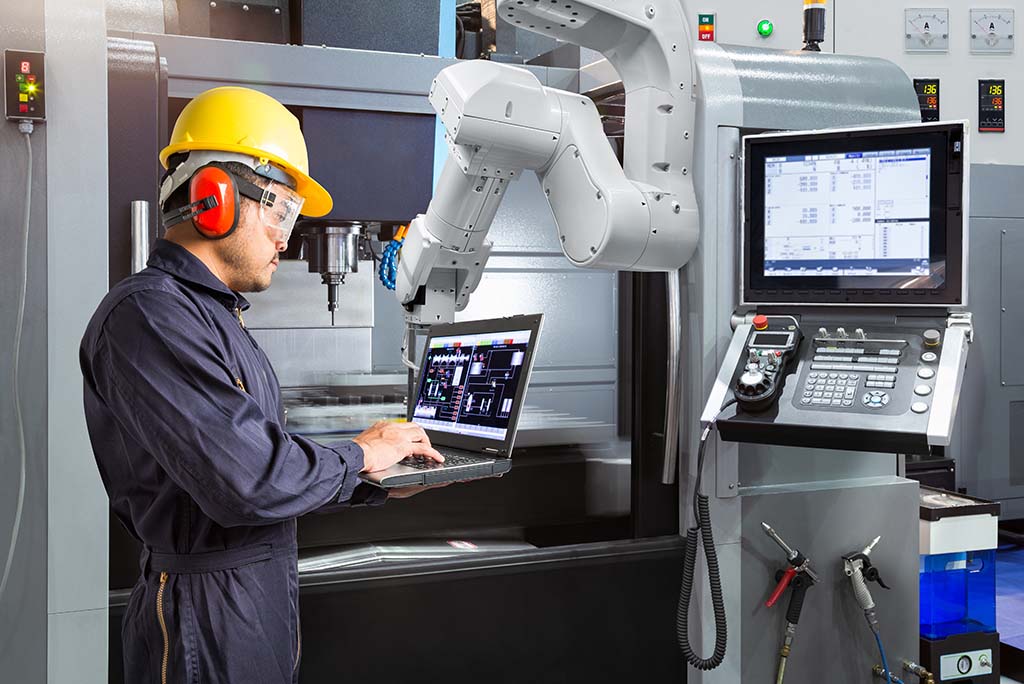 Maintenance engineer using a laptop to control a robotic arm