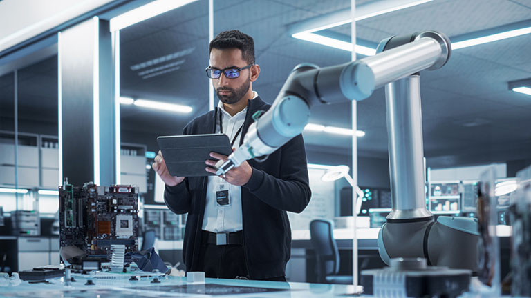 A man working on a tablet next to a robotic arm
