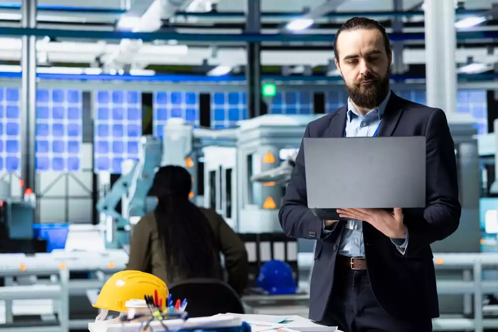 Man in a suit holding a laptop in a factory