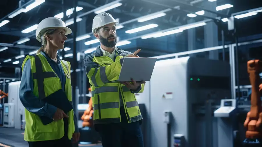 Manufacturing engineers discussing production performance while using a laptop on the factory floor