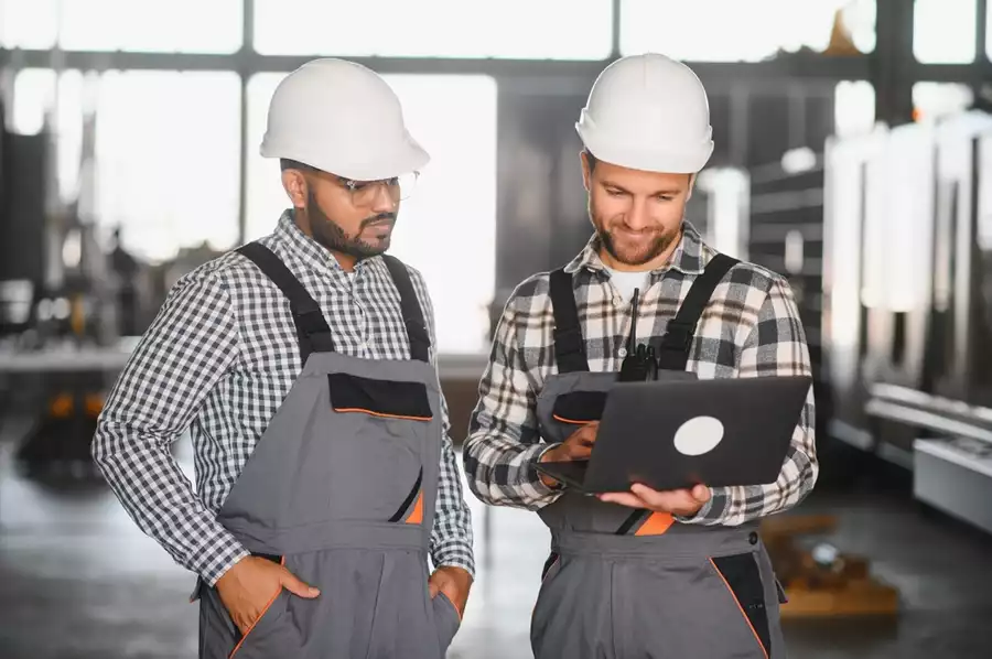 Two factory workers in overalls reviewing manufacturing operations in an industrial facility
